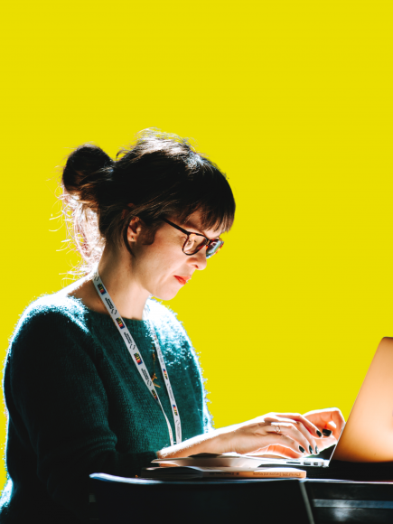Picture of a woman writing on a computer on a yellow background