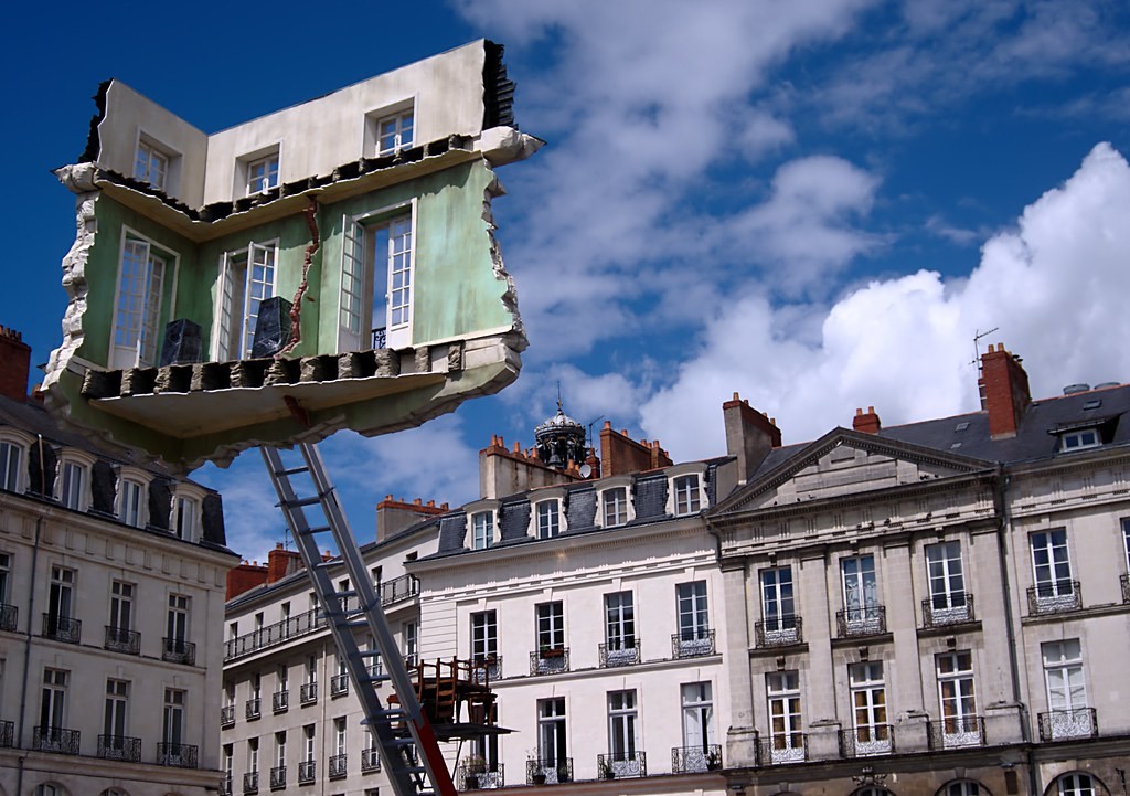 @Monte-meubles – L’ultime déménagement Picture of a torn apartment transported on a machine in the middle of a city square
