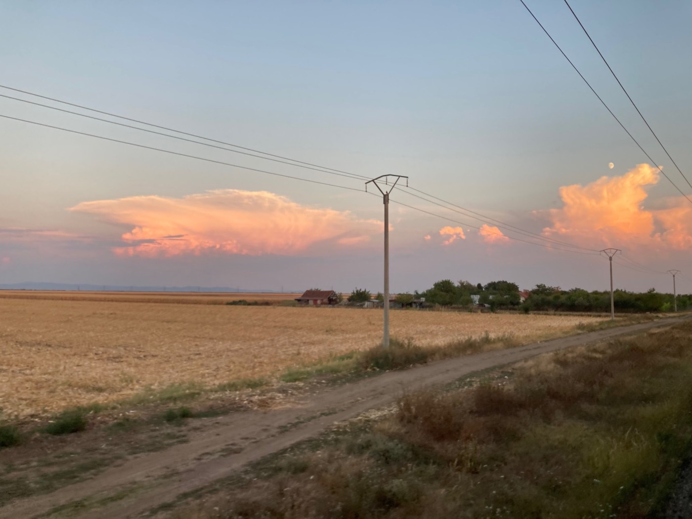 view of brownish fields, electric wires and a pretty sky of sunkissed clouds aaginst the blue