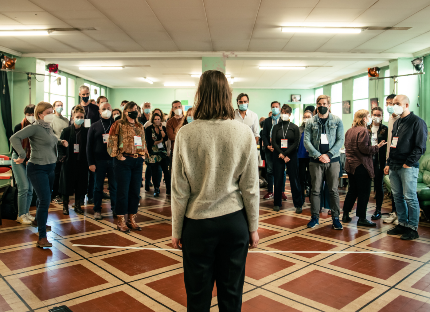 Picture of a woman with brown hair facing a crowd of masked participants at IETM Lyon 2021