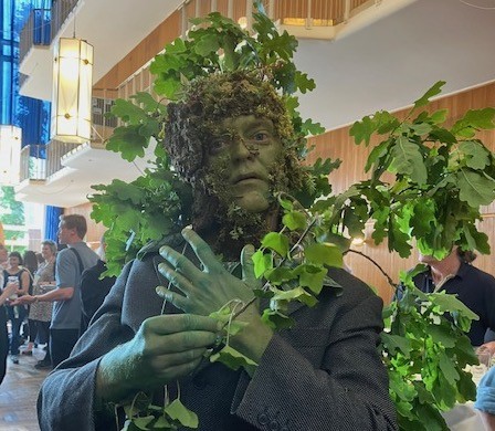 a close up of a performer dressed as a tree, painted freen with live foliage in City Hall