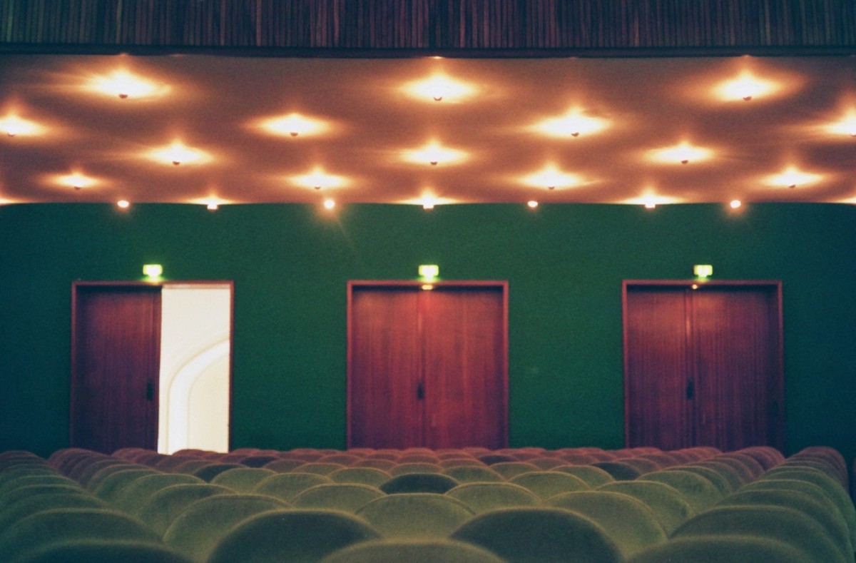 Picture of three doors at the back of a venue with green seats and green walls, with the left door open and the other two closed