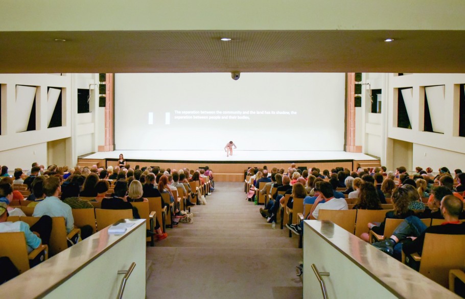 Participants of IETM Porto 2018 facing a stage where a man performs a performance