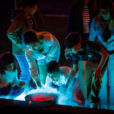 A group of young people looking down at a bucket filled with smoke which is lit in blue lighting