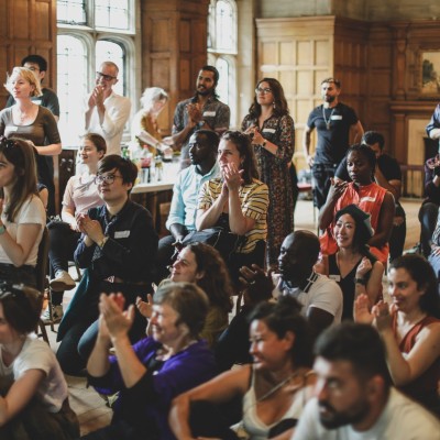 Join us! A large group of migrant artists at a celebration, clapping and looking inspired