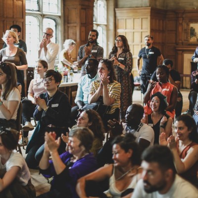 A large group of migrant artists at a celebration, clapping and looking inspired