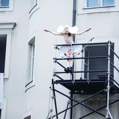 actor on balcony dressed in white spreading her arms like an angel
