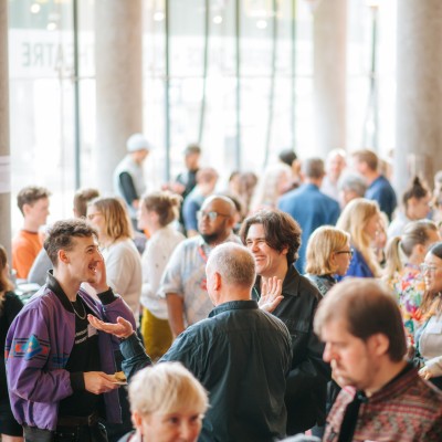 Arts professionals network in a large space with light spilling through tall glass windows