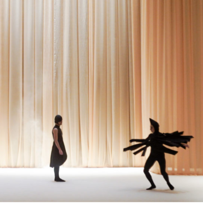 Two people on stage wearing black costumes, on a orange background